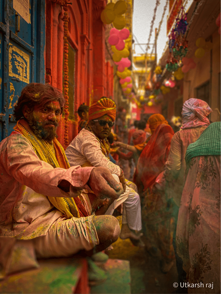 Man in white seated during Holi street celebrations
