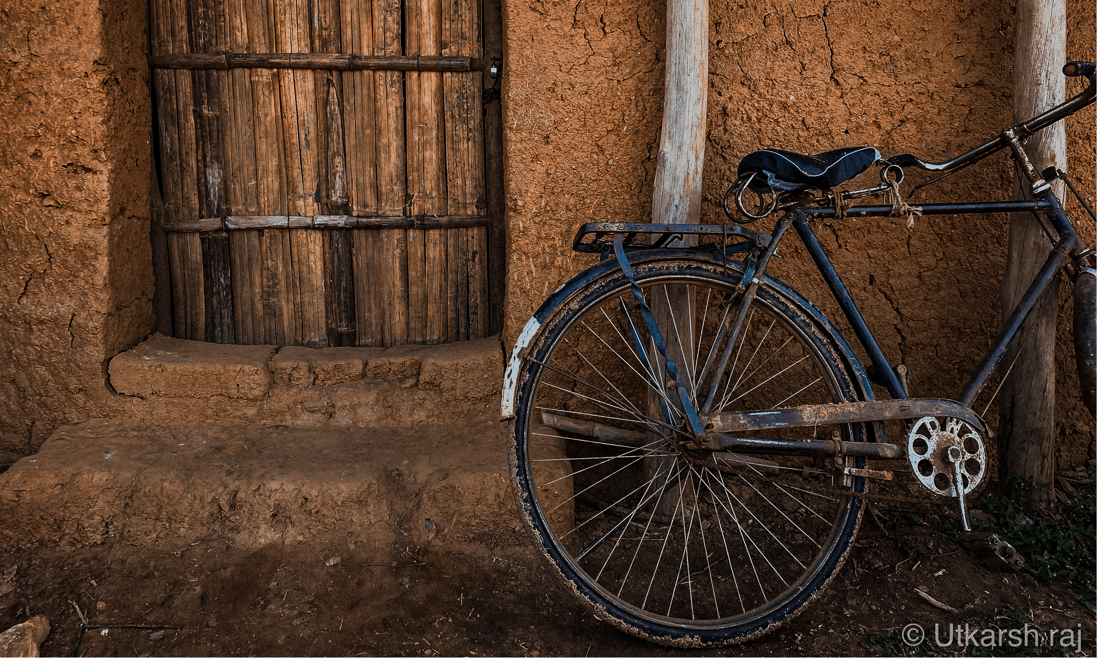 Old bicycle leaning against a mud-brick wall and bamboo door