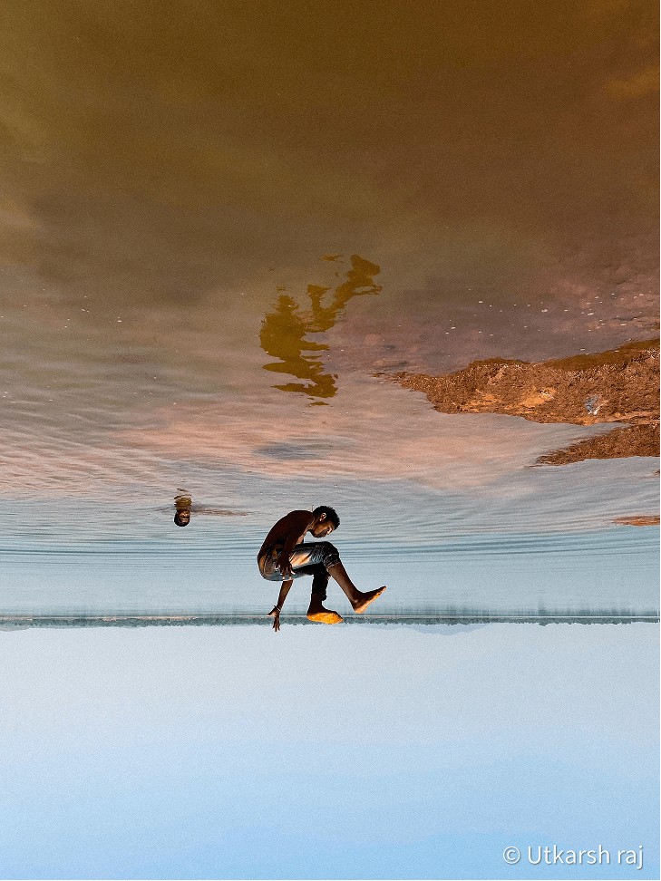 Figure at water's edge reflected in a mirror-still surface