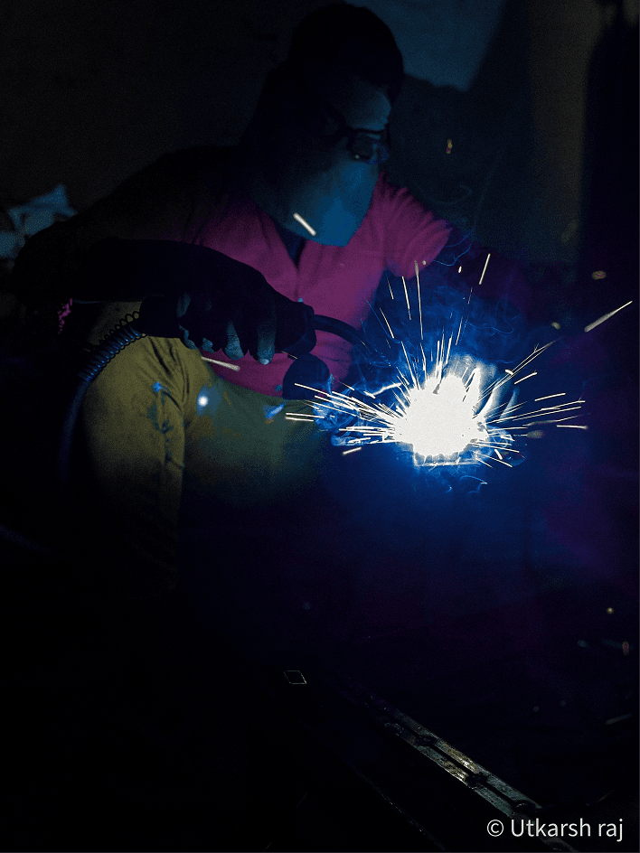 Welder at work, blue sparks exploding in the dark