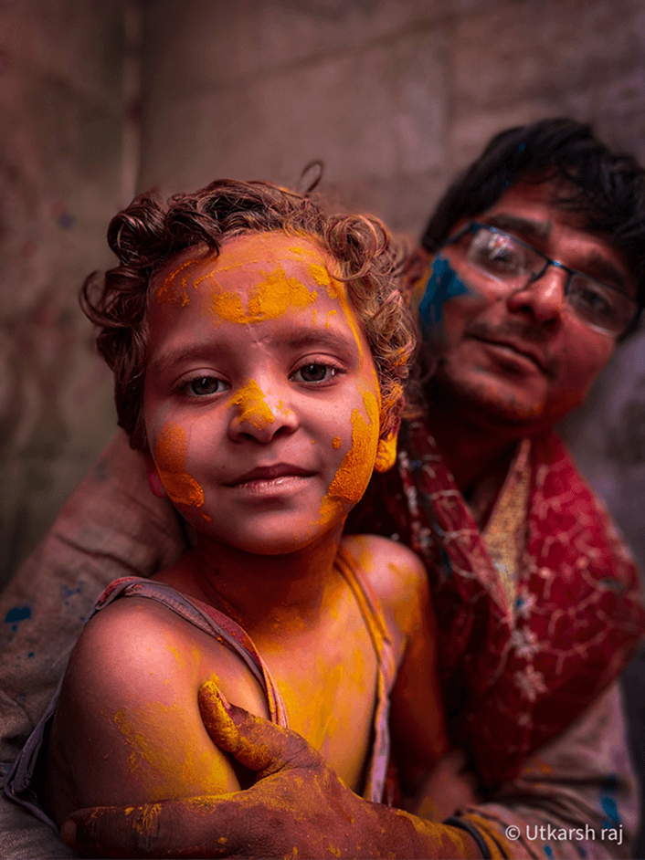 Child covered in Holi colours, father behind
